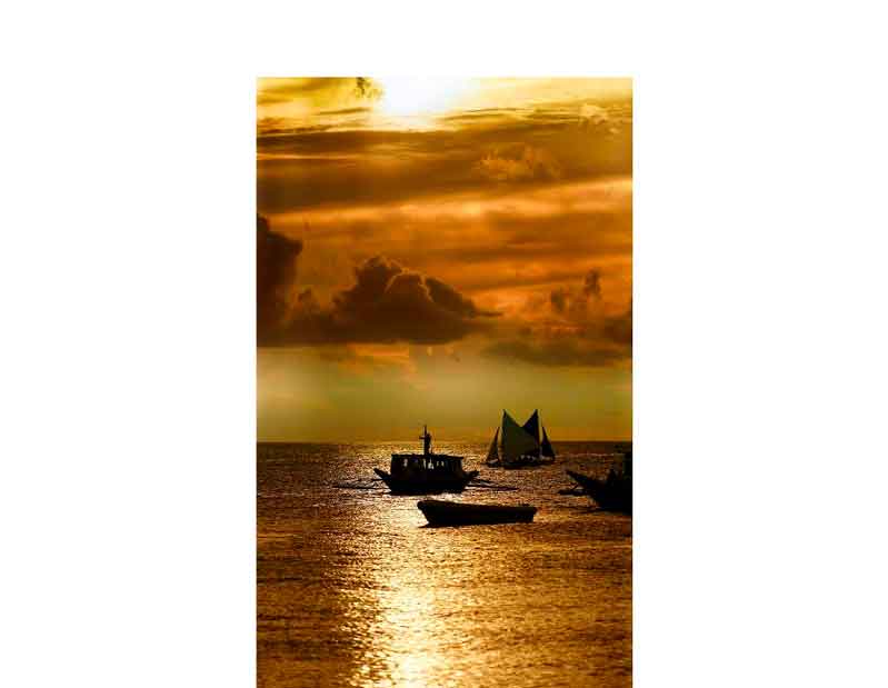 Ein malerischer Sonnenuntergang mit mehreren Segelbooten auf dem Meer, goldene Lichtreflexe auf den Wellen.